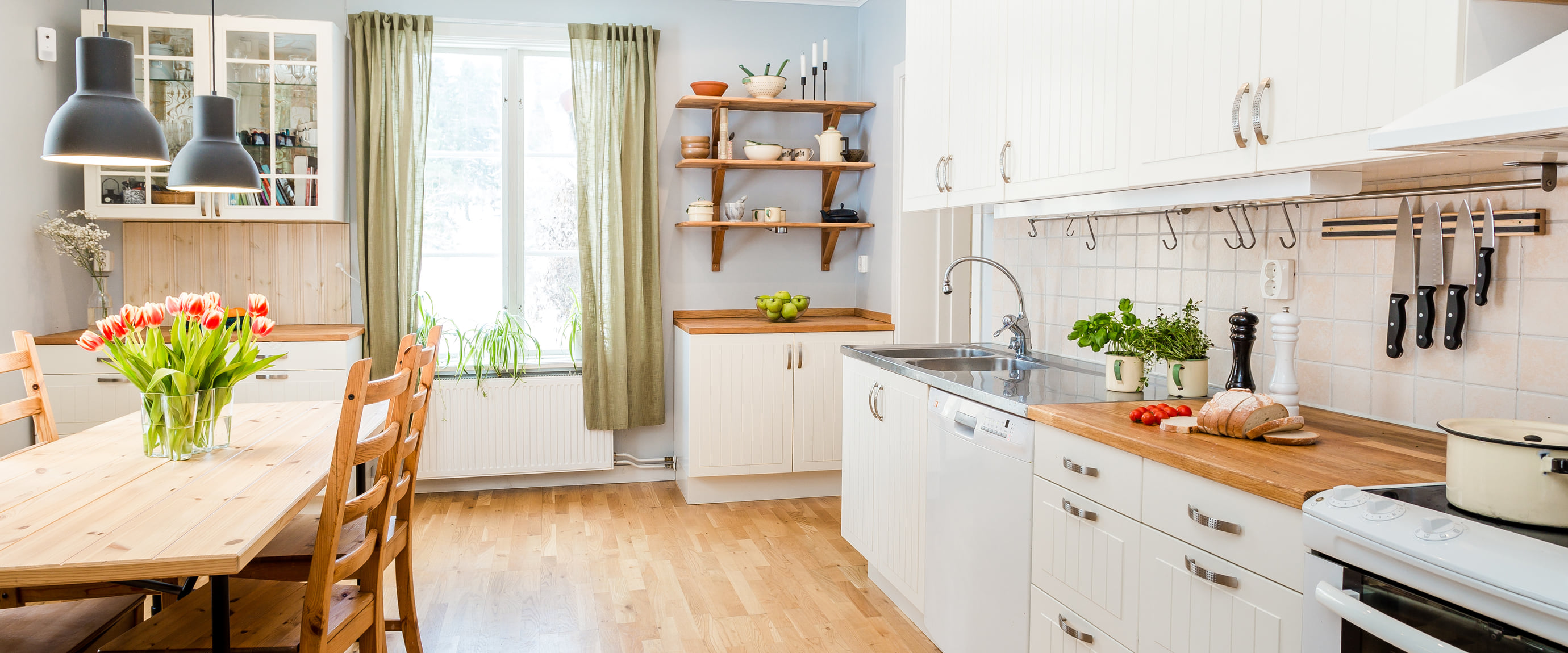 A bright, freshly cleaned kitchen and dining room with tidy wood counters, a farmhouse table and fresh tulips